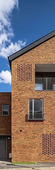 Three-storey modern brick house with a perforated brick screen and dark metal balcony against a blue sky